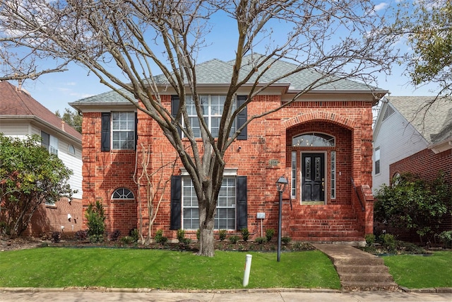 view of front of house with a front yard, brick siding, and a shingled roof