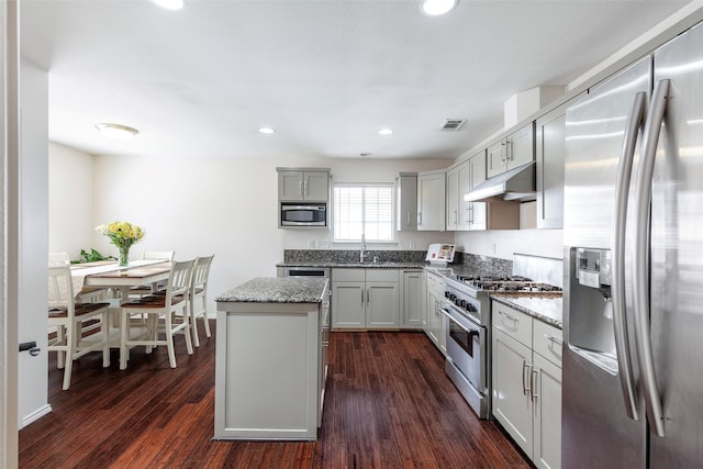 kitchen featuring a kitchen island, dark wood-type flooring, light stone countertops, under cabinet range hood, and appliances with stainless steel finishes