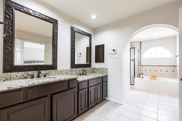 bathroom featuring tile patterned flooring, baseboards, double vanity, a bath, and a sink