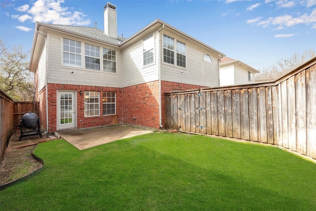 back of property with a yard, a patio area, brick siding, and a chimney