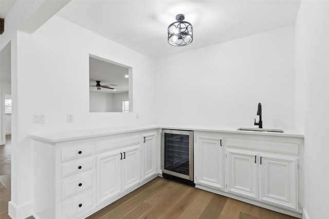 kitchen featuring beverage cooler, light countertops, wood finished floors, white cabinets, and a sink