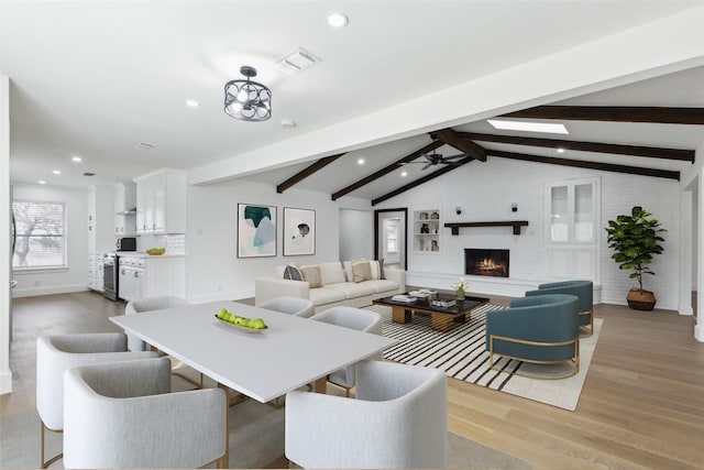 interior space featuring light wood finished floors, vaulted ceiling with beams, recessed lighting, a fireplace, and a ceiling fan