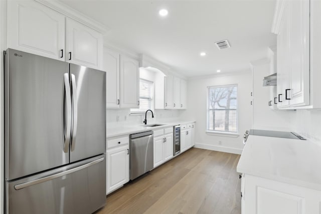 kitchen with light wood finished floors, beverage cooler, light countertops, appliances with stainless steel finishes, and white cabinets