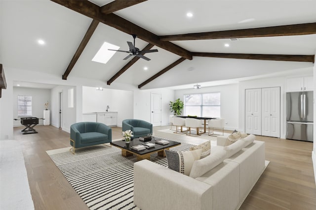 living area featuring lofted ceiling with skylight, ceiling fan, baseboards, and light wood-style floors