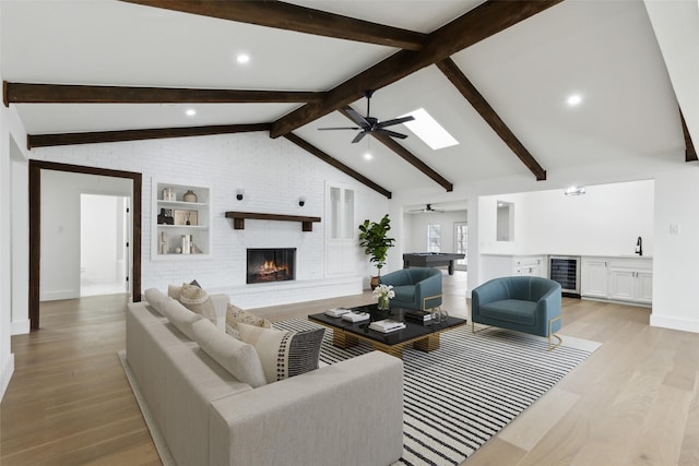 living area with light wood finished floors, a brick fireplace, wine cooler, lofted ceiling with skylight, and a ceiling fan