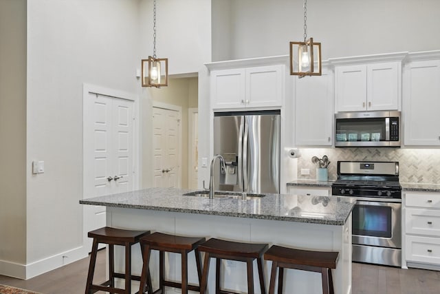 kitchen with a kitchen bar, a kitchen island with sink, a sink, backsplash, and appliances with stainless steel finishes