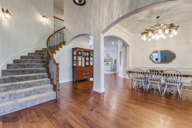 dining room featuring hardwood / wood-style floors, arched walkways, crown molding, baseboards, and stairs