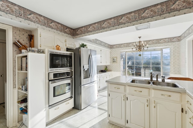 kitchen with wallpapered walls, light countertops, an inviting chandelier, stainless steel appliances, and a sink