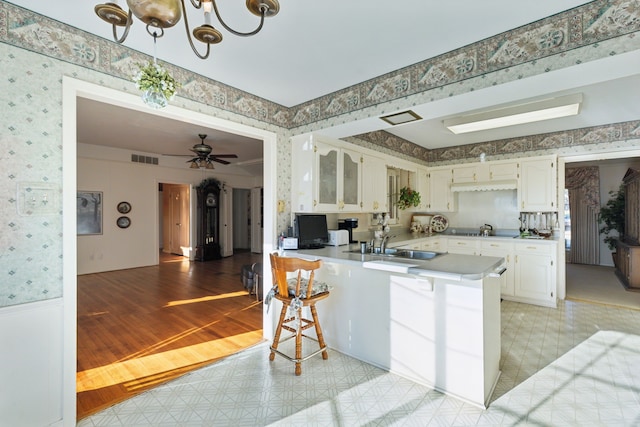 kitchen featuring wallpapered walls, a peninsula, visible vents, and a sink