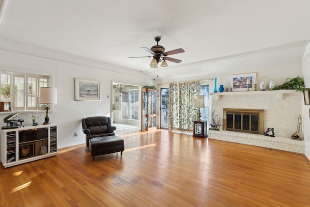 living area with a fireplace, a ceiling fan, and wood finished floors