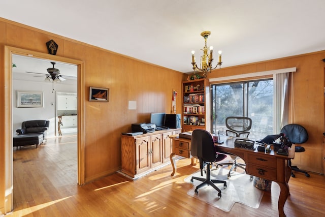 office area with light wood-type flooring, wooden walls, and ceiling fan with notable chandelier