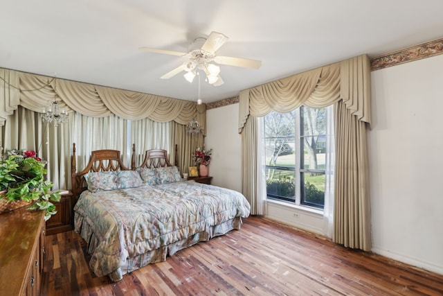 bedroom featuring ceiling fan with notable chandelier, wood finished floors, and baseboards