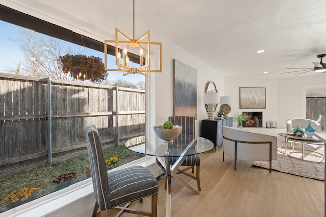 dining room with a ceiling fan, plenty of natural light, wood finished floors, and a lit fireplace