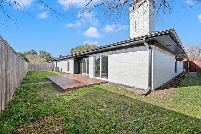 back of house with a lawn, a deck, a fenced backyard, brick siding, and a chimney