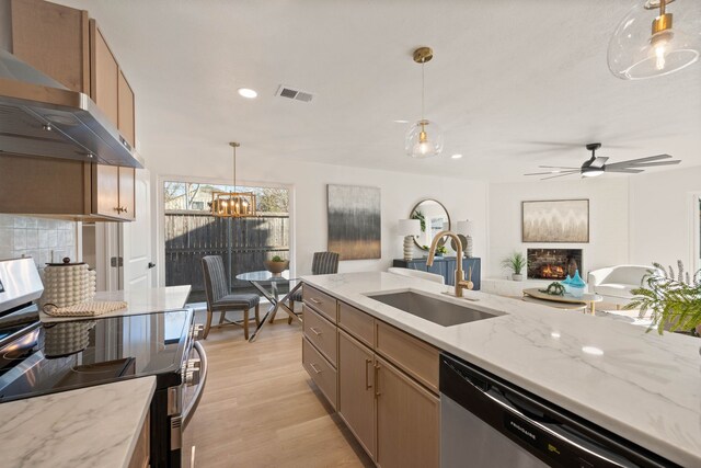 kitchen with visible vents, a sink, stainless steel appliances, a lit fireplace, and wall chimney exhaust hood