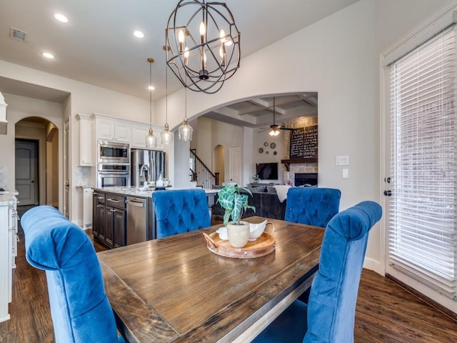 dining room with visible vents, a stone fireplace, dark wood-style floors, arched walkways, and coffered ceiling