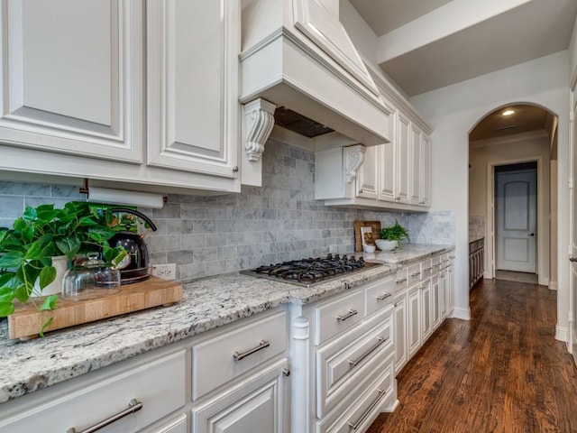 kitchen with tasteful backsplash, arched walkways, stainless steel gas stovetop, custom exhaust hood, and white cabinetry