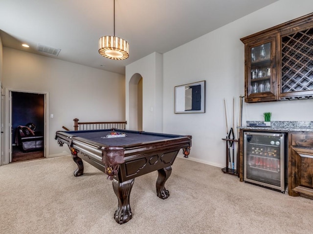 rec room with a dry bar, beverage cooler, light colored carpet, and arched walkways