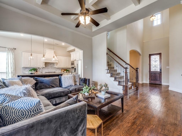 living room featuring dark wood-style floors, stairway, arched walkways, baseboards, and a towering ceiling