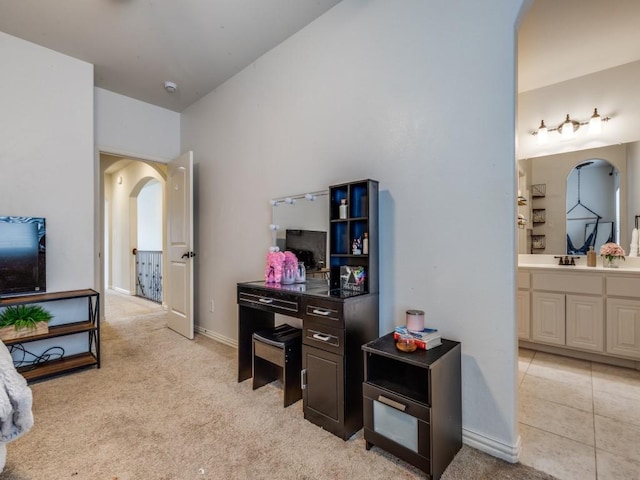 interior space featuring connected bathroom, baseboards, light carpet, arched walkways, and a sink