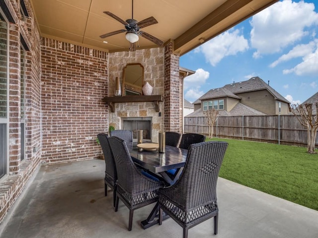 view of patio with outdoor dining space, an outdoor stone fireplace, a ceiling fan, and fence