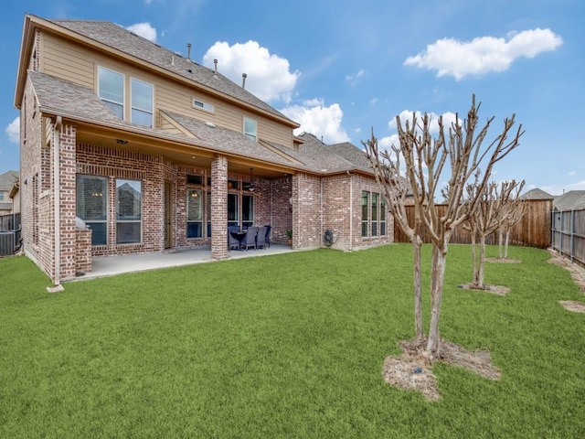 back of property featuring a fenced backyard, a yard, roof with shingles, brick siding, and a patio area