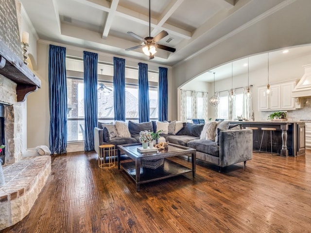 living area featuring arched walkways, coffered ceiling, a fireplace, and dark wood-type flooring