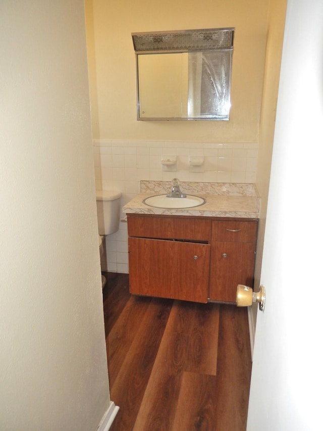 bathroom featuring a wainscoted wall, toilet, wood finished floors, tile walls, and vanity