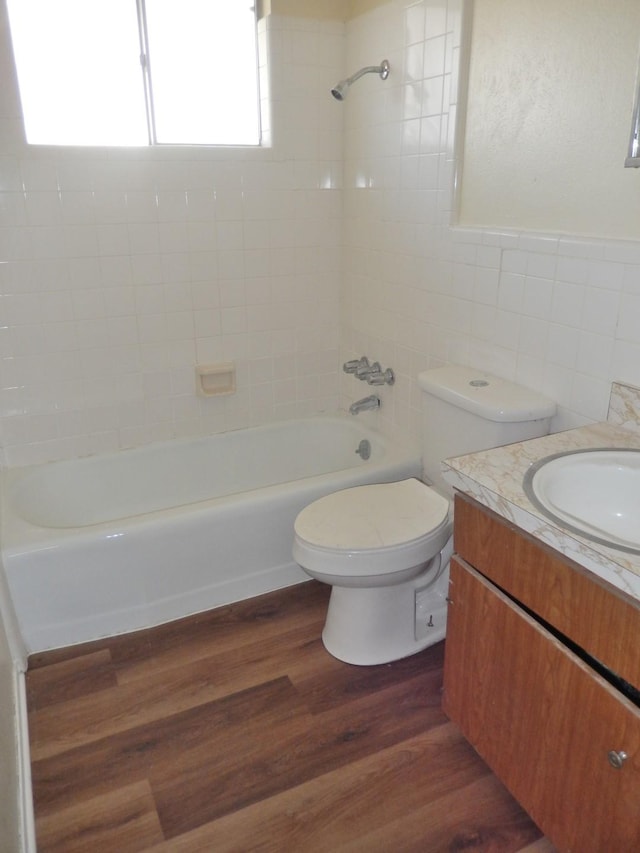 bathroom with toilet, wood finished floors, shower / bathing tub combination, tile walls, and vanity