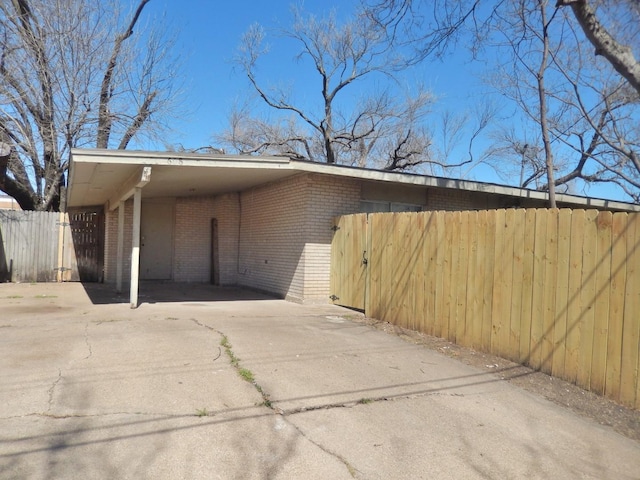 exterior space featuring an attached carport, fence, brick siding, and driveway