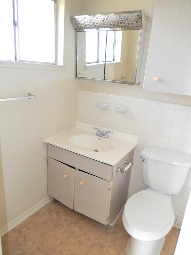 half bath featuring plenty of natural light, toilet, vanity, and tile walls