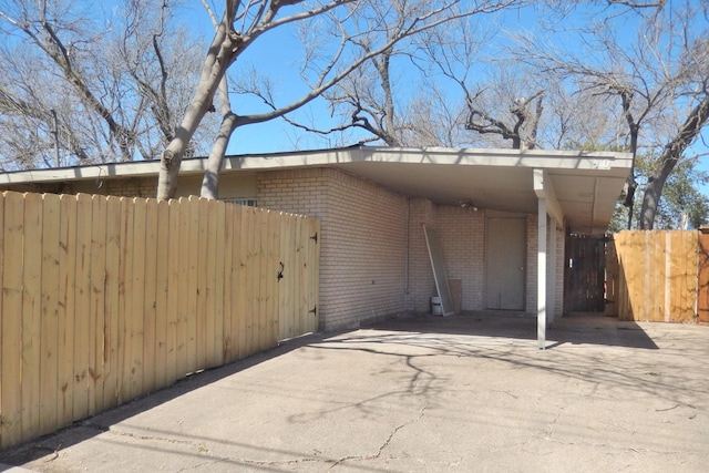 exterior space featuring brick siding, concrete driveway, a carport, and fence