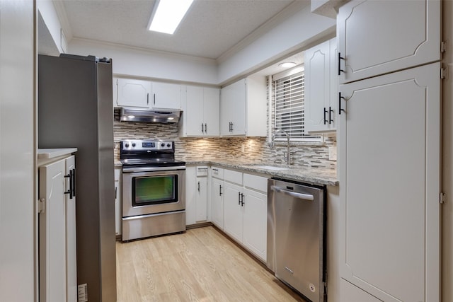 kitchen featuring a sink, stainless steel appliances, under cabinet range hood, crown molding, and light wood-type flooring