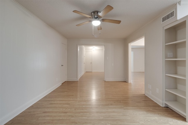 spare room with built in features, light wood-type flooring, visible vents, and crown molding