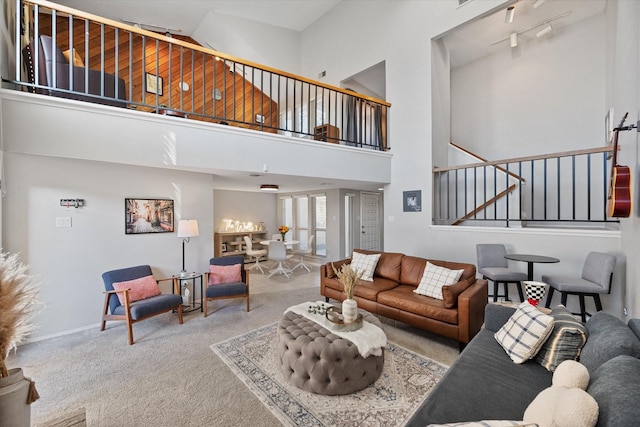 carpeted living room featuring rail lighting, baseboards, a towering ceiling, and stairs