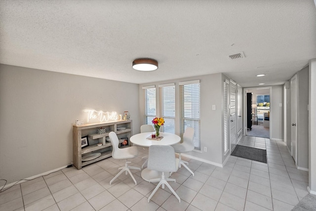 dining space with light tile patterned flooring, visible vents, a textured ceiling, and baseboards