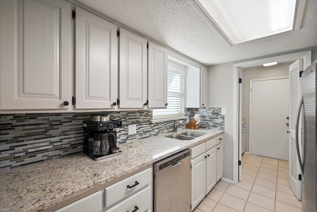 kitchen featuring a sink, a textured ceiling, appliances with stainless steel finishes, light tile patterned flooring, and white cabinets