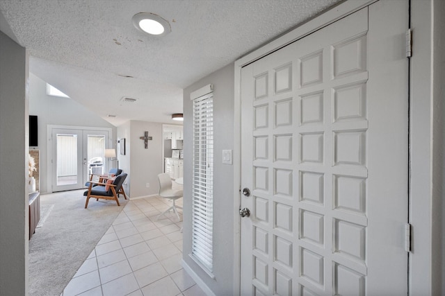 foyer with baseboards, light tile patterned floors, light carpet, french doors, and a textured ceiling