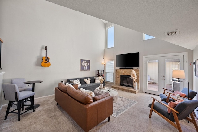 living area featuring visible vents, light carpet, a fireplace with raised hearth, a textured ceiling, and french doors