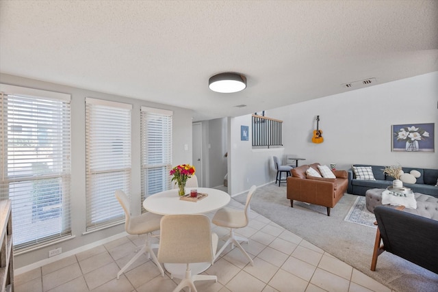 dining space with visible vents, a textured ceiling, light tile patterned floors, baseboards, and light colored carpet