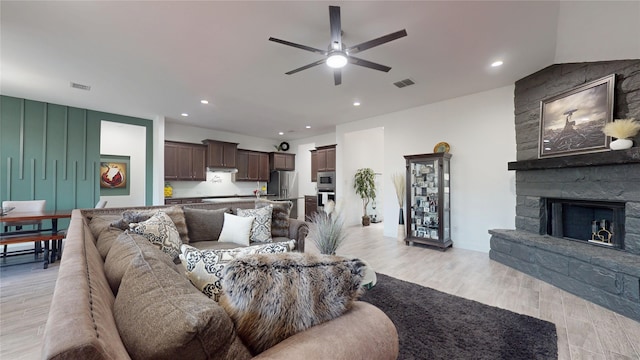 living area with a stone fireplace, recessed lighting, light wood finished floors, and ceiling fan