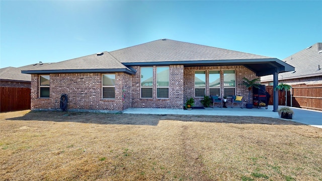 rear view of house with brick siding, a lawn, a shingled roof, and fence