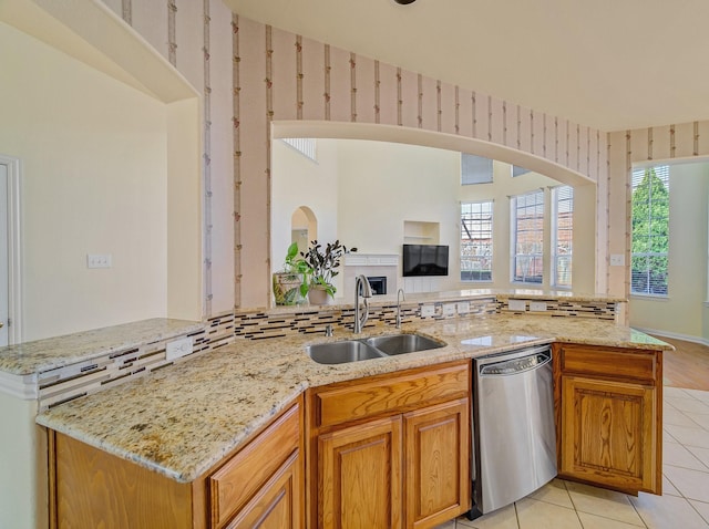 kitchen with a sink, stainless steel dishwasher, wallpapered walls, light tile patterned floors, and light stone countertops