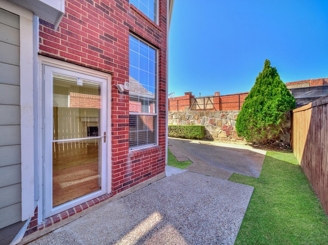 doorway to property featuring brick siding, a patio area, and fence