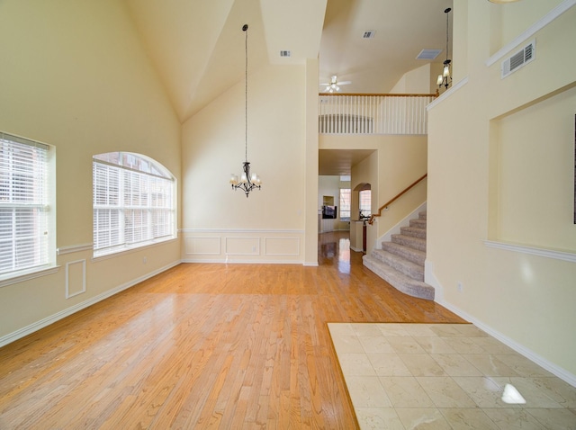 entrance foyer with visible vents, stairs, ceiling fan with notable chandelier, wood finished floors, and high vaulted ceiling