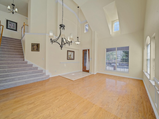 unfurnished living room featuring wood finished floors, baseboards, a high ceiling, stairs, and a notable chandelier