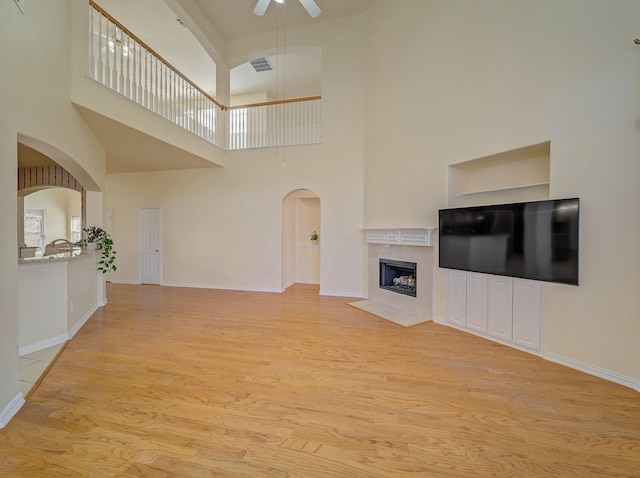 unfurnished living room with a ceiling fan, visible vents, light wood finished floors, arched walkways, and a high end fireplace