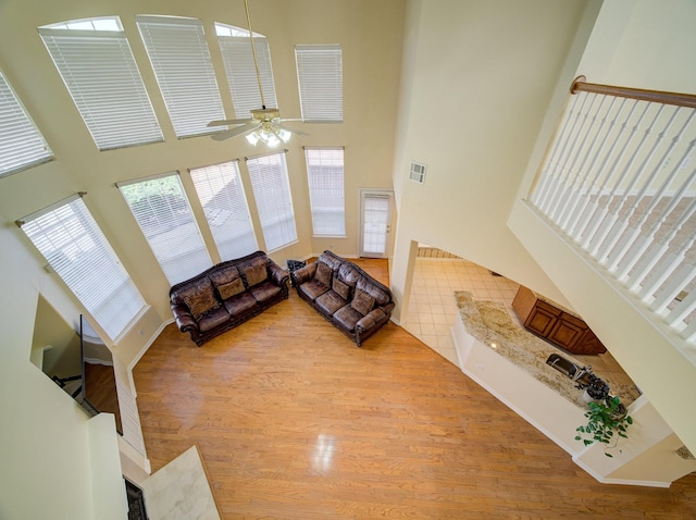 living area featuring wood finished floors, visible vents, a towering ceiling, and ceiling fan