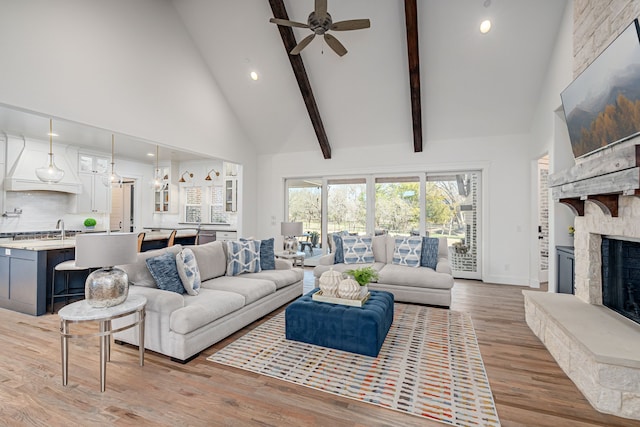 living area with beamed ceiling, high vaulted ceiling, a fireplace, and light wood finished floors