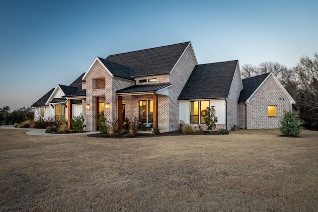 view of front facade featuring a standing seam roof, a front lawn, brick siding, and metal roof